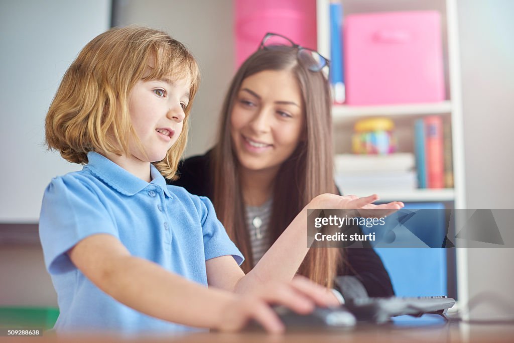 Primary schoolgirl using a  computer with her teacher