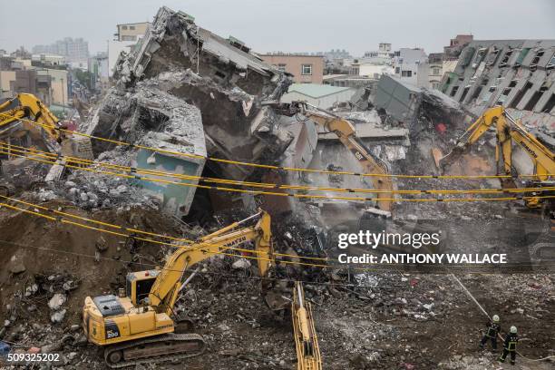 Firefighters hose down falling rubble to prevent dust from rising as excavators are used during the search and rescue operation at the Wei-Kuan...