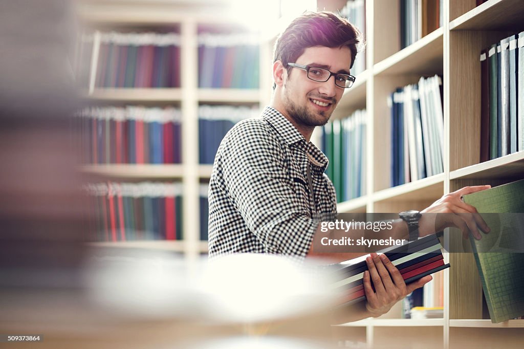 Smiling student choosing books in library and looking at camera.