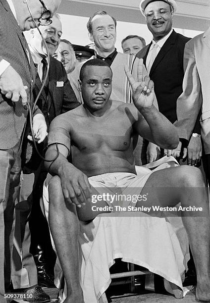 Sonny Liston holding up two fingers, gesturing second round knockout, during his medical check-up before his fight vs Cassius Clay at the Cypress...