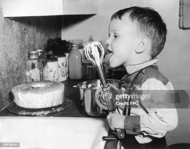 Small boy licks cake mixture off a whisk, circa 1955.