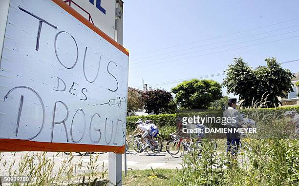 The pack passes by a placart "Tous des Drogues" and a policeman during the second stage of the Dauphine-Libere cycling race between Bron and...