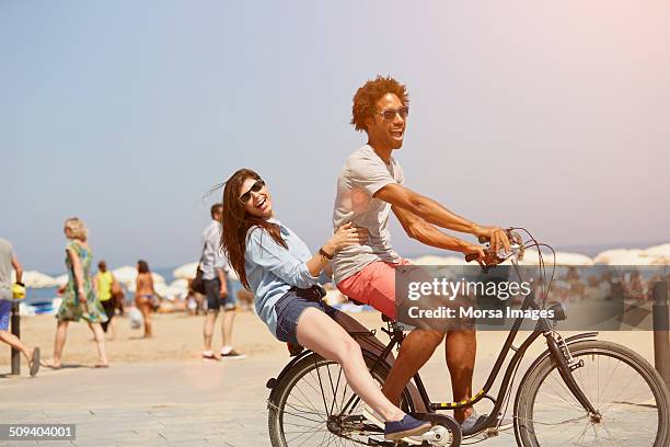 couple riding bicycle at beach - barcelona day photos et images de collection