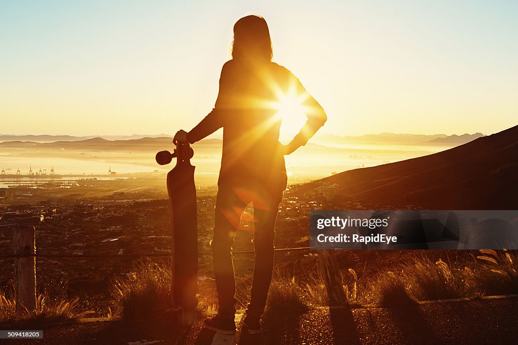 Longboarder silhouetted by rising sun on Table Mountain contour path