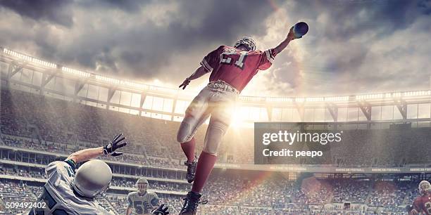 american football player jumps to catch ball during game - catching stock pictures, royalty-free photos & images