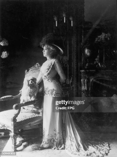 An elegant lady poses in her parlour with a lapdog, circa 1910.