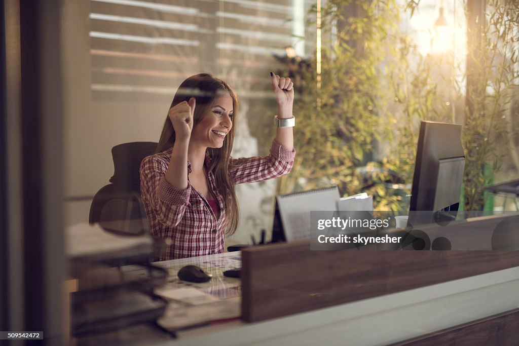 Joyeuse femme d'affaires célébrant un succès au bureau.