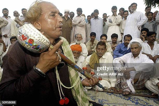 An elderly Pakistani singer plays a traditional musical instrument as he sings infront of an audience near the "Lahore Fort" in Lahore, 14 June 2004....