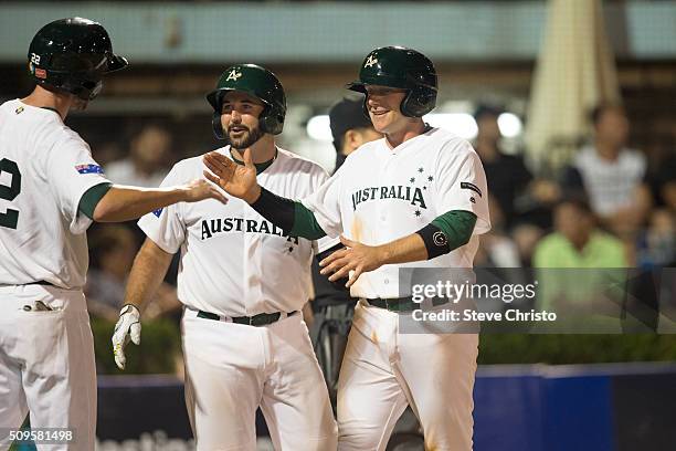 Luke Hughes of Team Australia is greeted by teammates Stefen Welch and Allan De San Miguel after scoring a run during Game 2 of the World Baseball...