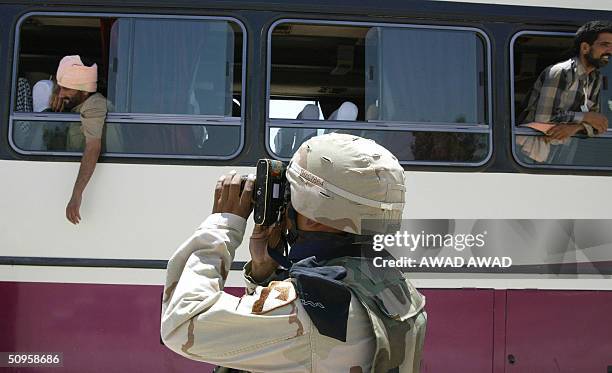 Military police takes a snap shot of an Iraqi man looking out of the window of a bus following his release from the Abu Ghraib prison, west of...