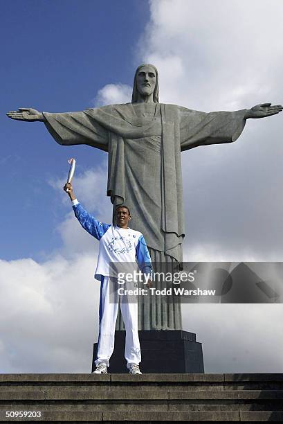 Joaquin Cruz, Brazilian Olympic track competitor, carries the Olympic Flame atop Corcovado Mountain in front of the Christ the Redemer statue during...