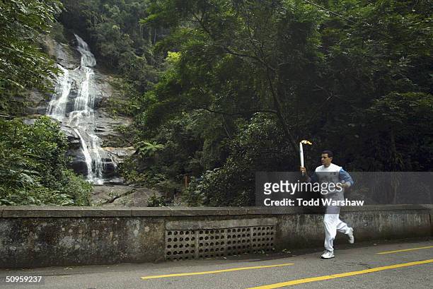 Torchbearer Agberto Guimaras carries the Olympic Flame past Tijuca Falls during the ATHENS 2004 Olympic Torch Relay on June 14, 2004 in Rio De...