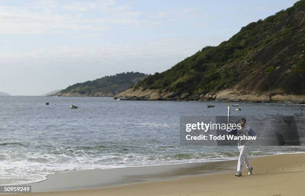 Torchbearer Agberto Guimaraes carries the Olympic Flame on Praia Vermelha during the ATHENS 2004 Olympic Torch Relay on June 14, 2004 in Rio De...