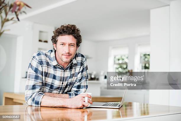 portrait of man having coffee while using laptop - chemise à carreaux photos et images de collection