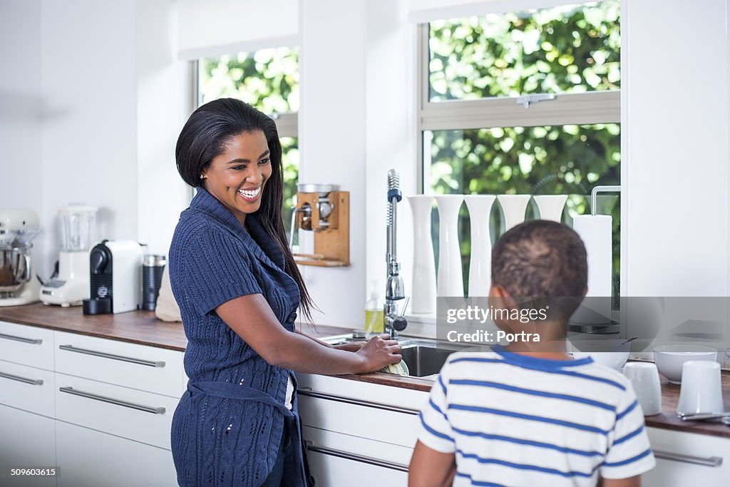 Happy mother cleaning dishes with son in kitchen