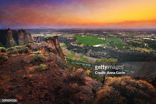 woman in blue dress stands on edge of plateau at smith rock summit at sunset, oregon - smith rock state park stock-fotos und bilder