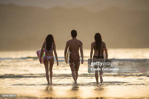 friends walking into the water to surf at sunset - hanalei national wildlife refuge stock pictures, royalty-free photos & images