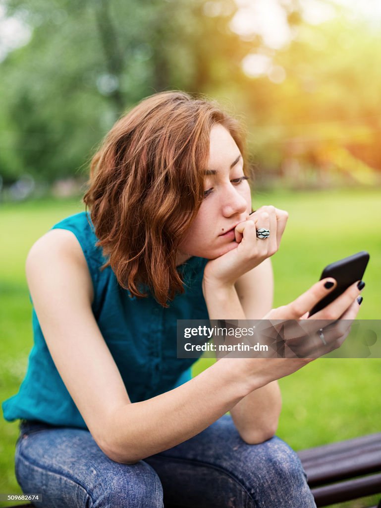 Teenage girl texting on smartphone in the park