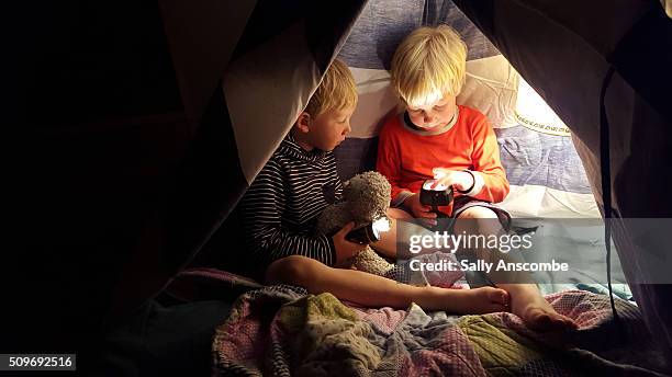 Two children playing in a tent by torch light