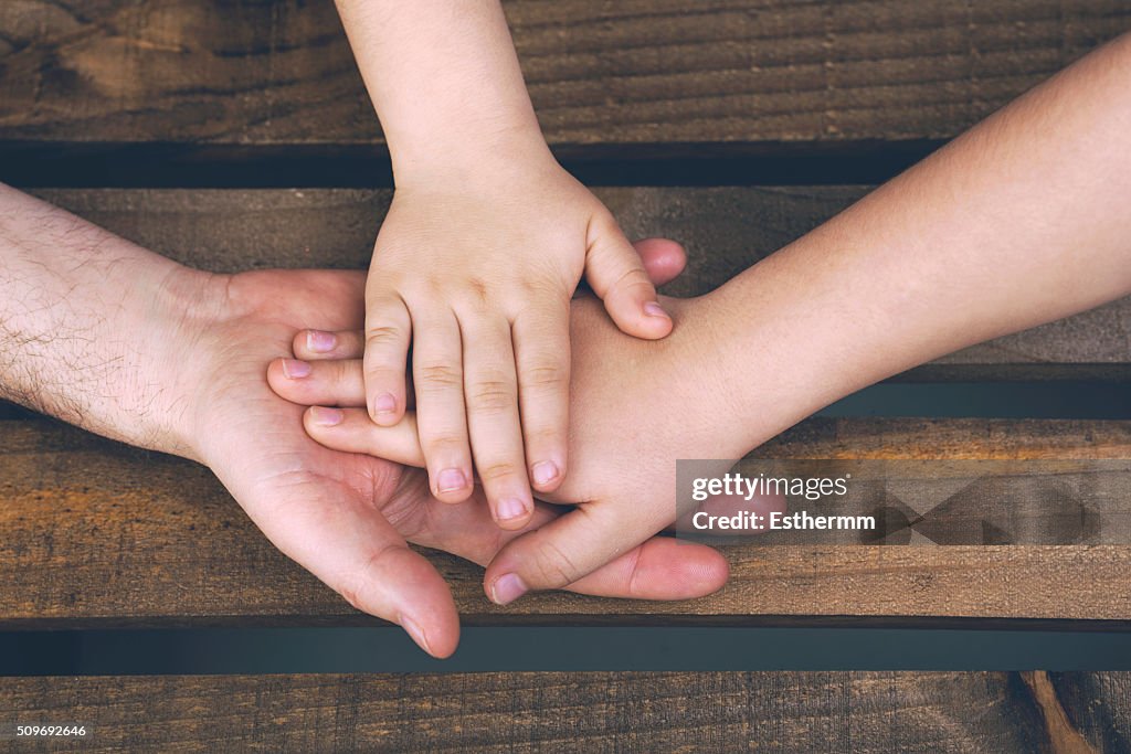 Hands of a parent with their children on a wooden table