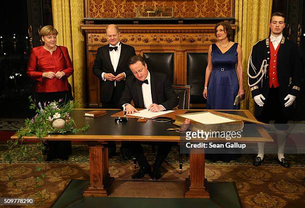 British Prime Minister David Cameron signs the Golden Book of Hamburg as German Chancellor Angela Merkel Hamburg's Mayor Olaf Scholz and his wife...