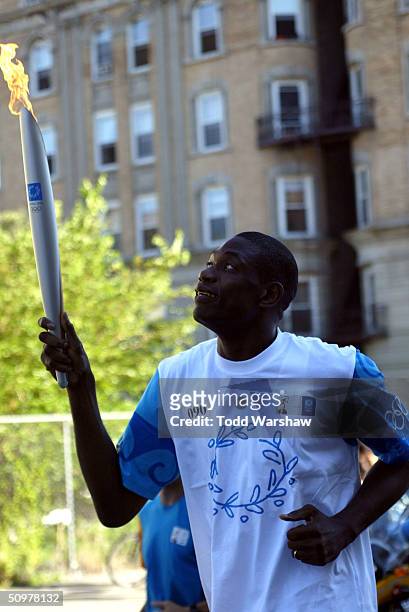 Torchbearer and NBA player Dikembe Mutumbo carries the Olympic Flame during Day 15 of the ATHENS 2004 Olympic Torch Relay on June 19, 2004 in New...