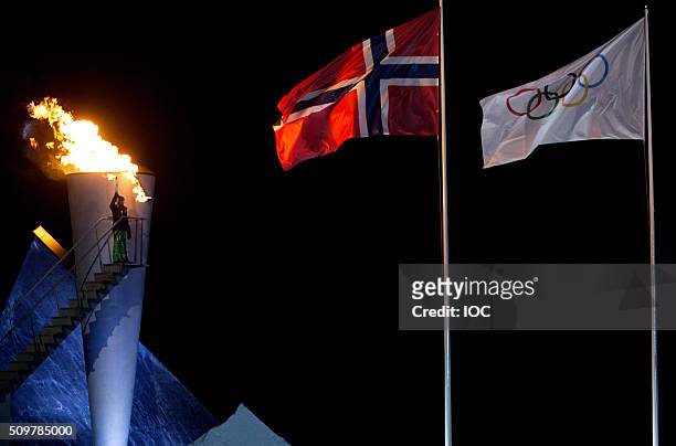 In this handout image supplied by the IOC, The Norwegian Flag and the Olympic Flag fly over Lysgrdsbakkene Ski Jumping Arena as the flame of the...