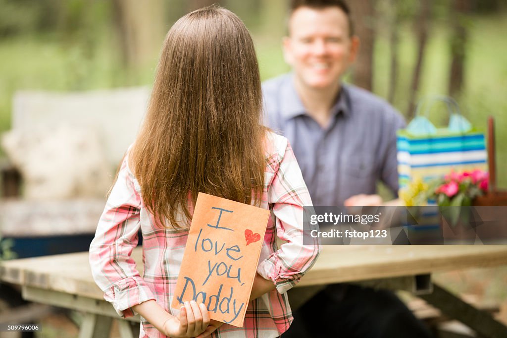 Daughter gives dad handmade Father's Day card. Outdoors. Child, parent.