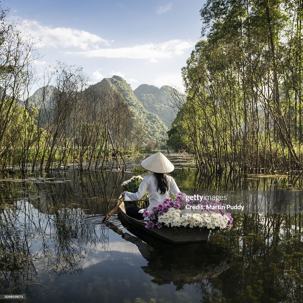 Woman rowing small boat, carrying flowers