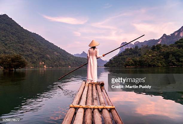 woman punting bamboo raft across lake - vietnam photos et images de collection
