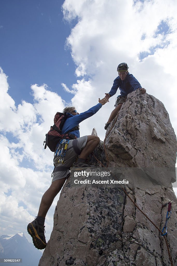 Climber extends helping hand to partner, pinnacle