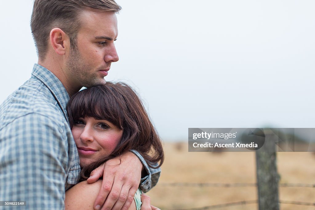 Couple embrace at edge of rural field, fog