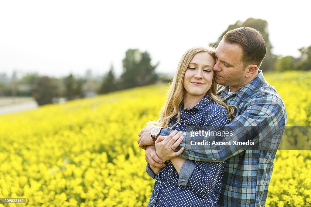 Couple embrace in field of yellow flowers