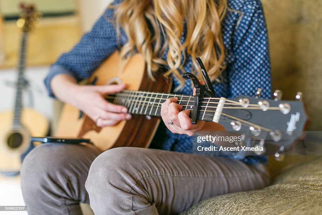 Woman plays guitar on living room couch