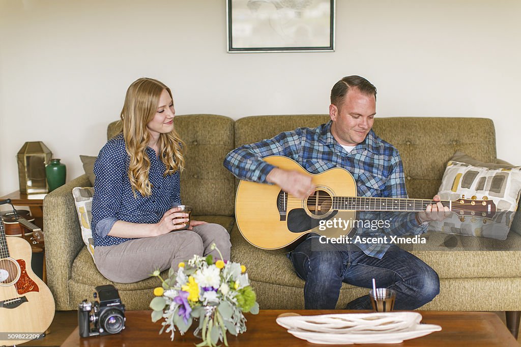 Man plays guitar, living room couch, woman watches