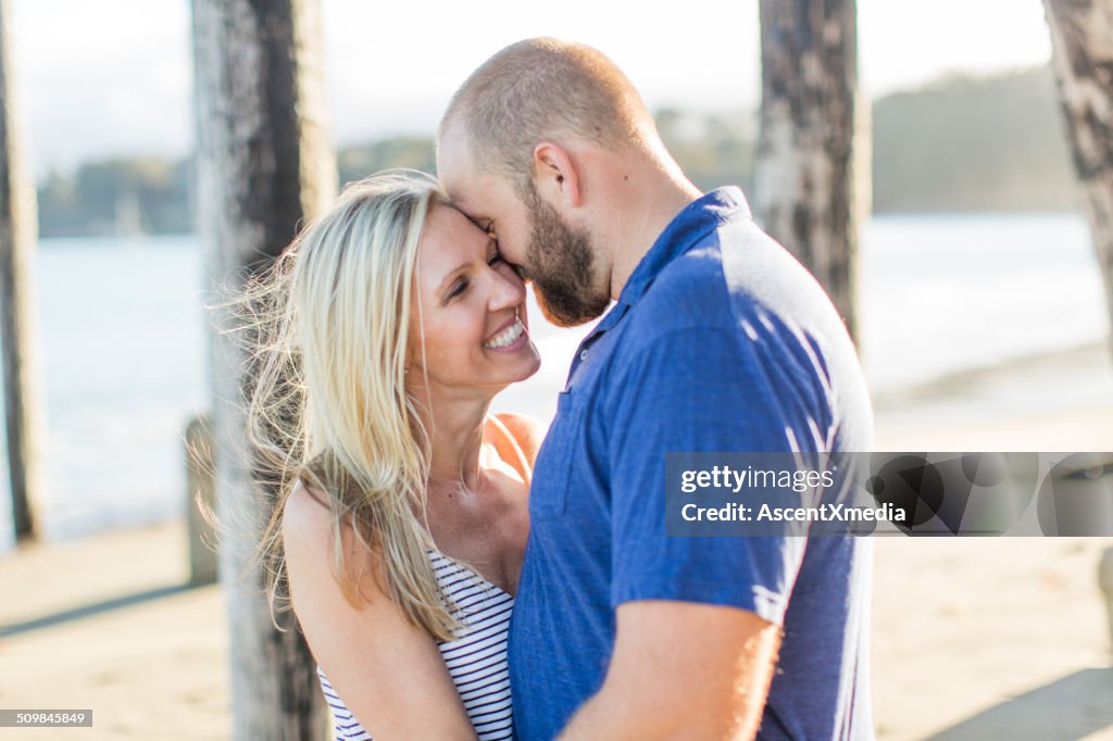 Couple embrace on beach below wooden pier