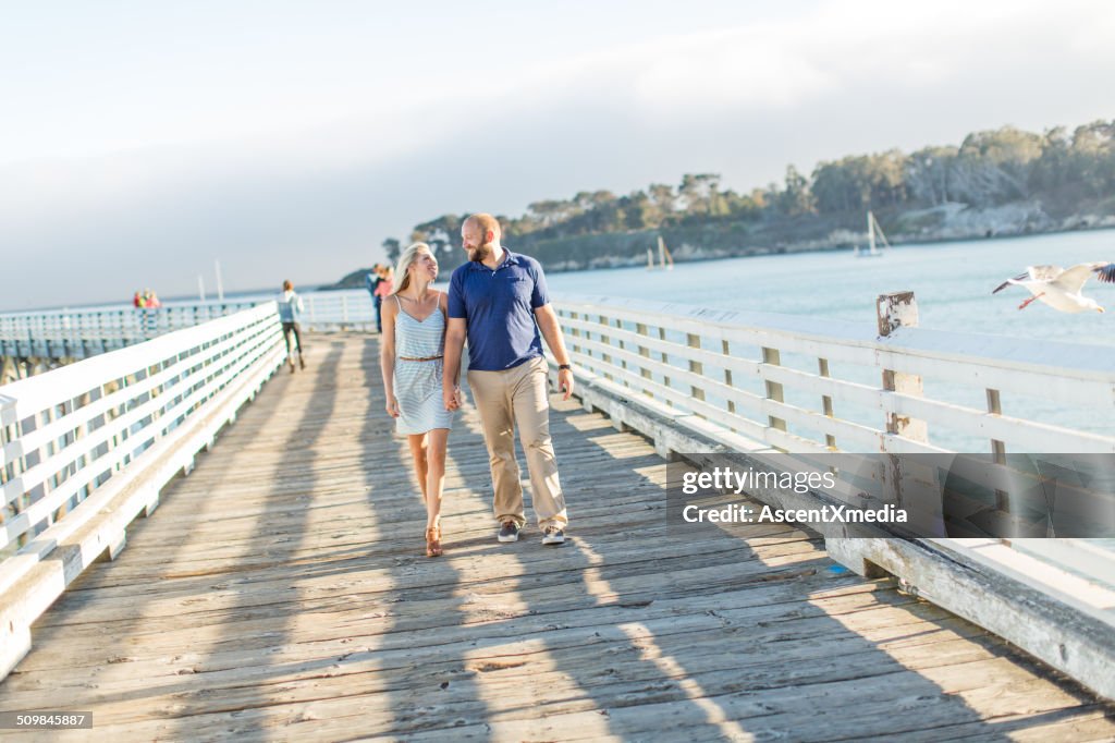 Couple walk along wooden pier at seaside