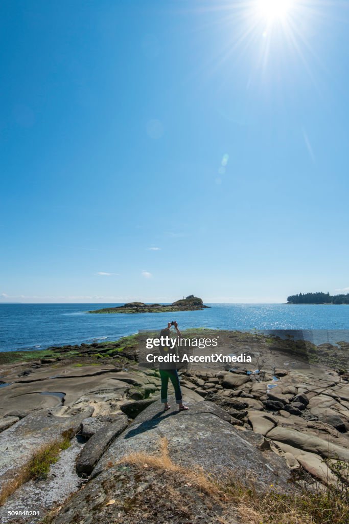 Woman takes smart phone pic form rock shoreline