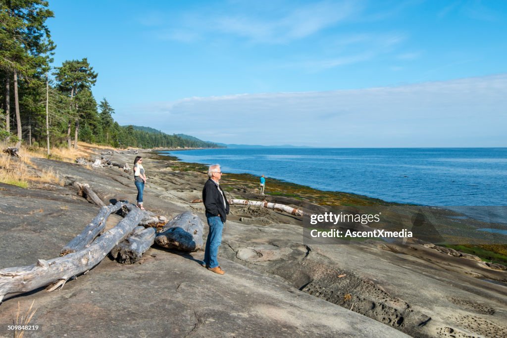 Three people stand on rocky shoreline, look to sea