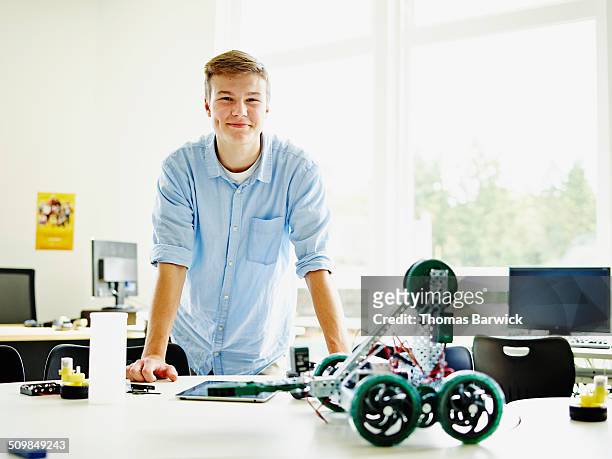 smiling male student in classroom with robot - schulbeginn stock-fotos und bilder