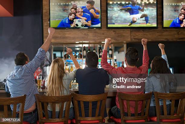 excited group of people watching the game at a bar - watching sport television stock pictures, royalty-free photos & images