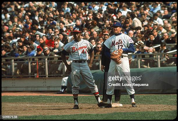 Hank Aaron of the Atlanta Braves focuses on the mound as first baseman Dick Stuart of the New York Mets holds him on during an MLB game at Shea...