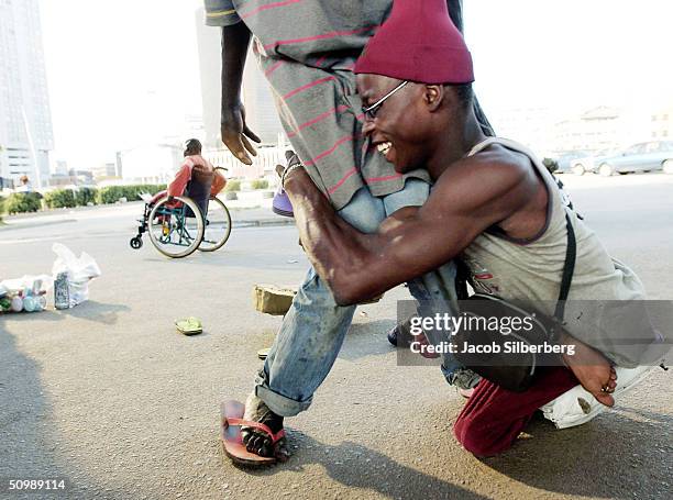 Man with polio wrestles with a friend November 1, 2003 in Lagos, Nigeria. The polio virus often causes wasting of the lower limbs. Kano led northern...