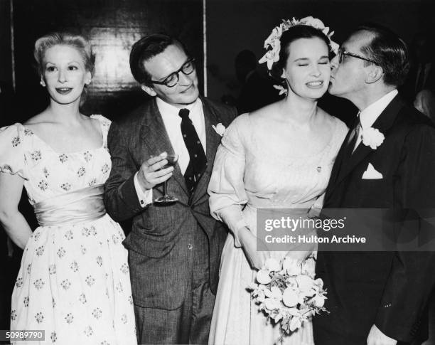 Blacklisted American playwright Sidney Kingsley kisses the cheek of American heiress and designer Gloria Vanderbilt as American film director Sidney...