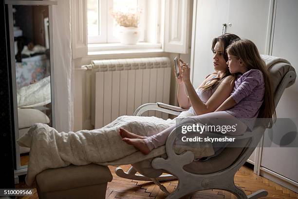 mother and daughter using cell phone together at home. - rocking chair stock pictures, royalty-free photos & images