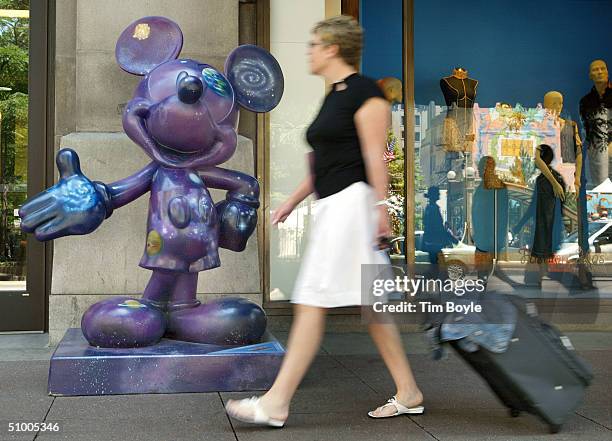 Woman walks past a Mickey Mouse statue titled "Space Mouse," designed by Tom Hanks, on State Street June 28, 2004 in Chicago, Illinois. This is one...