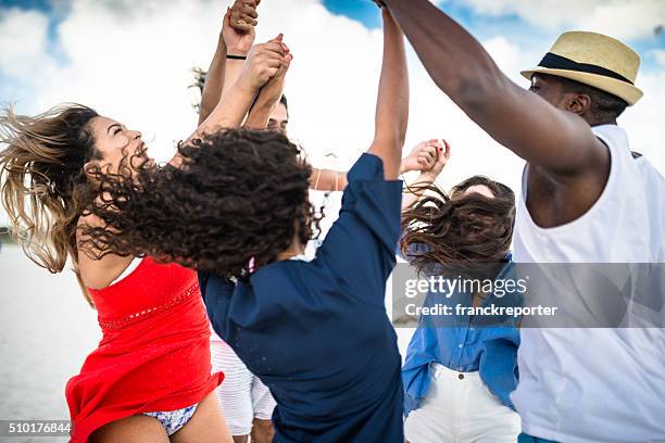 group of friends holding hands on the beach - lens flare young people dancing on beach stock pictures, royalty-free photos & images