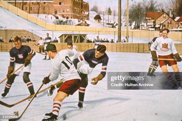An American hockey play attempts to sweep the puck away from a Canadian in a match between their two countries in the 1932 Lake Placid Olympics,...