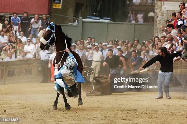 The jockey of the Onda , one of seventeen contrade or neighboroouds, holds onto his horse as he falls off in Piazza del Campo during the Palio horse...