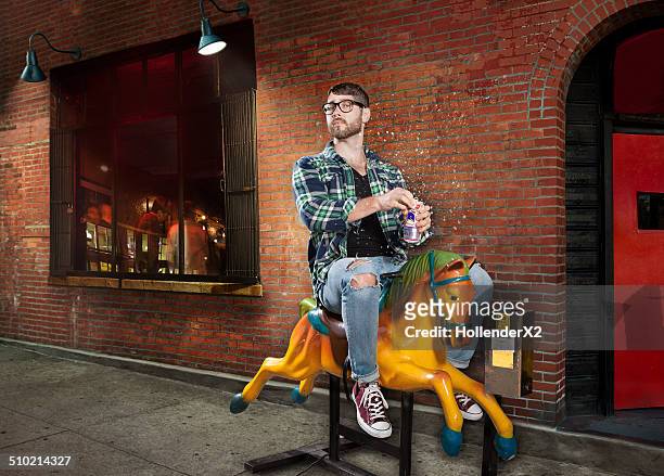 hipster man on mechanical horse drinking beer - young at heart stock-fotos und bilder